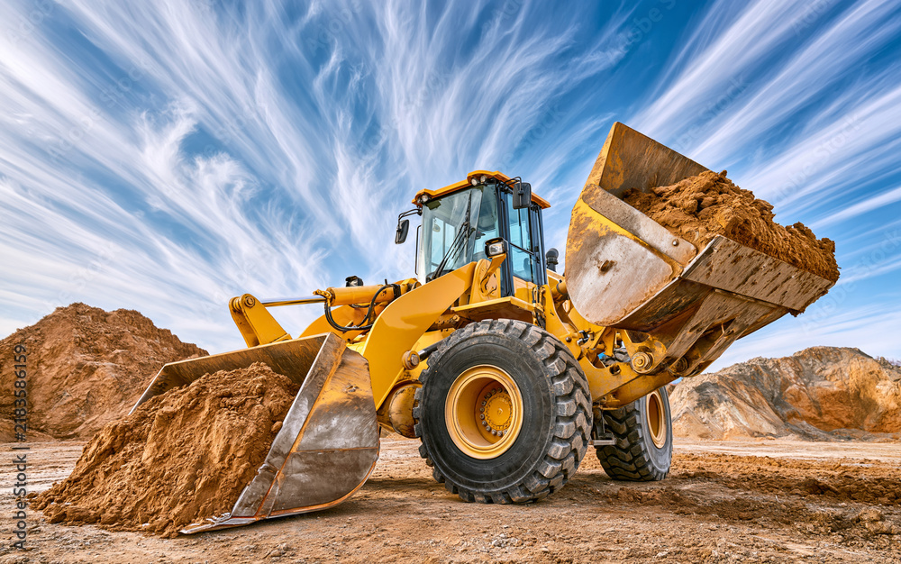 Fototapeta premium Yellow wheel loader scooping earth at construction site