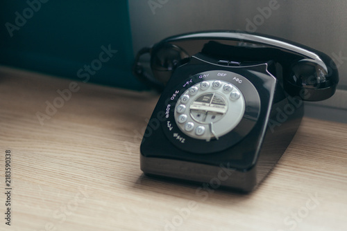 Vintage Black Rotary Telephone On Wooden Desk. Classic Communication Device With Dial Buttons And Glossy Finish.