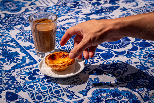 Hand reaching for pastel de nata custard tart with blue azulejo
