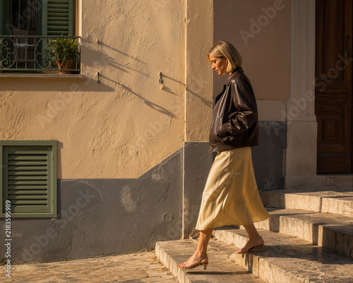 Stylish model in leather jacket walking down sunlit stone stairs