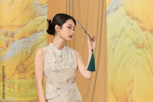 Fotografie Elegant woman in qipao holding tasseled fan with traditional Chinese backdrop