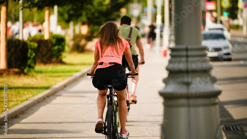 Cuadro en lienzo Woman riding a bicycle along a city sidewalk during summer, representing sustain