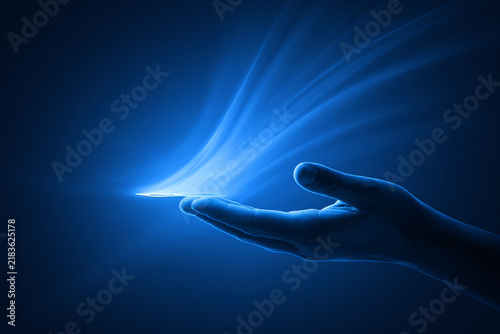 A graceful human hand holds a glowing ethereal object emitting radiant streams of brilliant blue light that curve elegantly upward into the dark mysterious void
