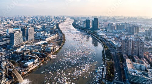 Aerial view of a city river covered with floating waste, showing urban pollution, environmental challenges, water contamination and the impact of human activity on natural ecosystems