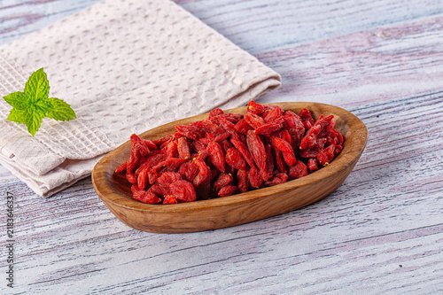 Obraz na plátně Dried red goji berries in wooden bowl on rustic painted wood surface with folded
