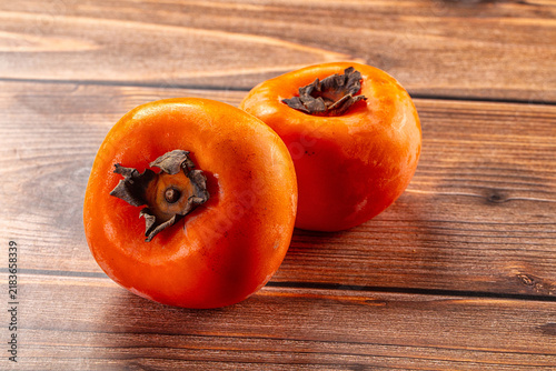Canvastavla Two ripe orange persimmons on rustic wooden surface, shallow depth of field, war