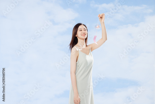 Obraz na plátně Smiling Young Woman Holding Wind Chime Under Blue Summer Sky