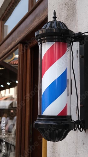 Close-up of a classic barber pole mounted outside a traditional barbershop, featuring the iconic red, white and blue spiral design