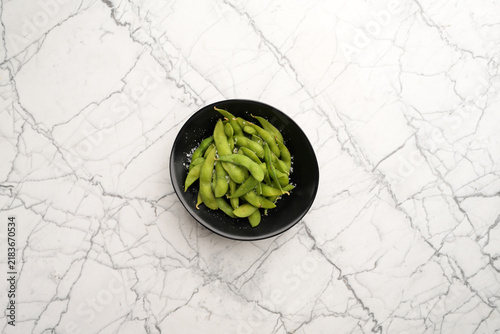 Steamed edamame beans sprinkled with sea salt in black bowl flat lay