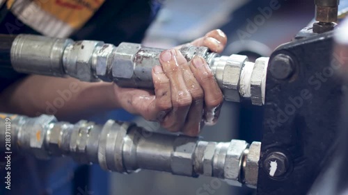 Static shot of technician hands connecting hydraulic hose coupler in mechanical workshop.
