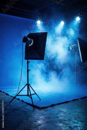 Photo studio with blue lighting and smoke. Professional lights and equipment ready for a creative photoshoot. Dynamic atmosphere for filming or artistic projects.