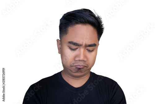 Fotografie Sad Indonesian man wearing a black t-shirt looking down with a disappointed and pouting expression against a white background