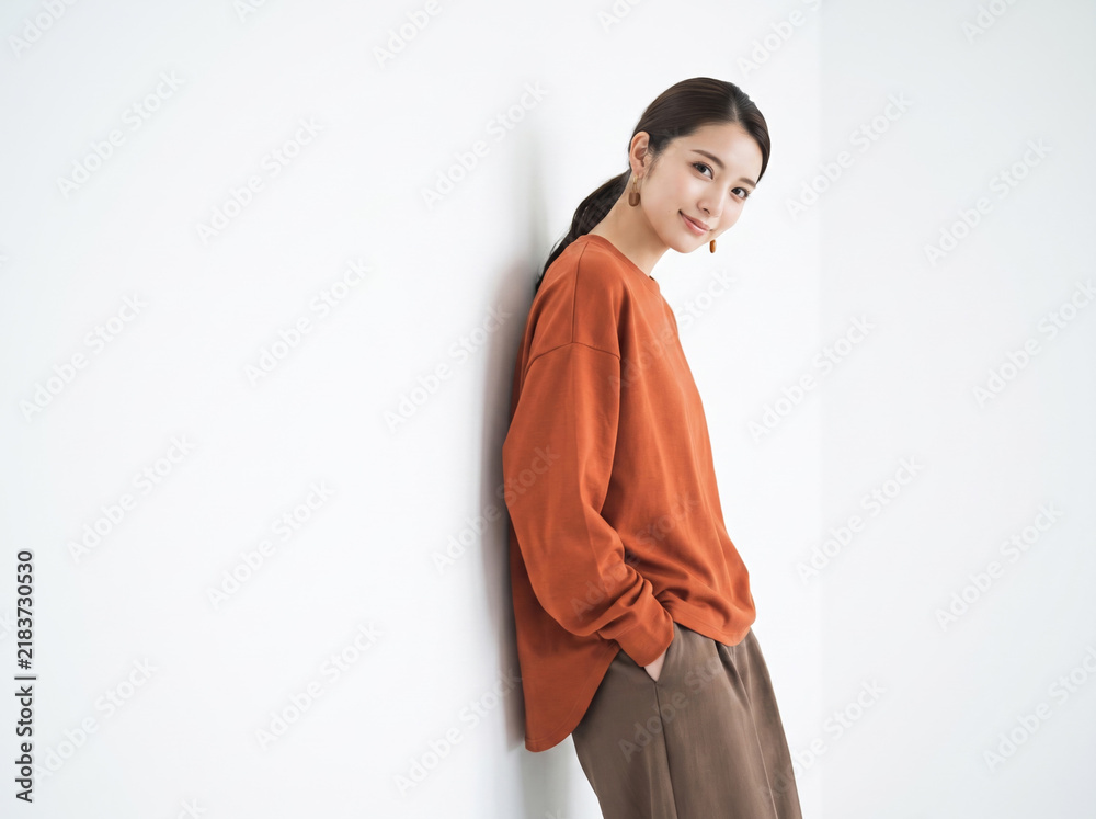Fototapeta premium 壁にもたれて笑顔を見せるオレンジ色のトップスを着た女性
