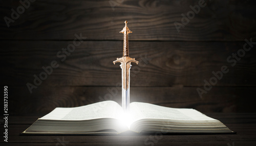 Open book Holy Bible on a dark background. Sword above the quiver symbolizes the Word of God. Prayer and spiritual struggle.