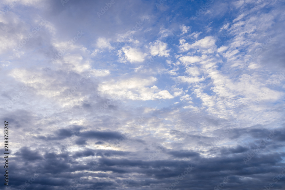 Fototapeta premium Bright blue daytime sky with soft white clouds,A wide-angle photograph of a serene blue sky filled with soft white and light grey cloud formations during the daytime. Bright natural sunlight filters 