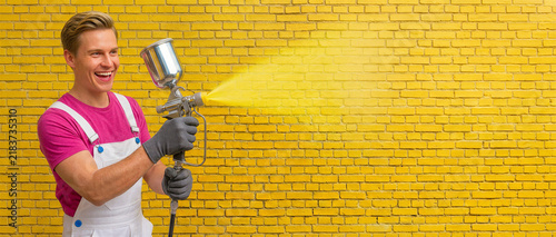 Man spraying yellow paint on brick wall with paint sprayer  