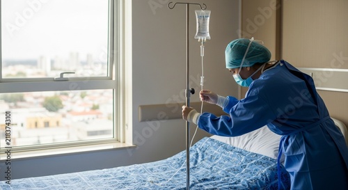 Medical professional in protective gear adjusts IV drip near hospital bed, symbolizing healthcare