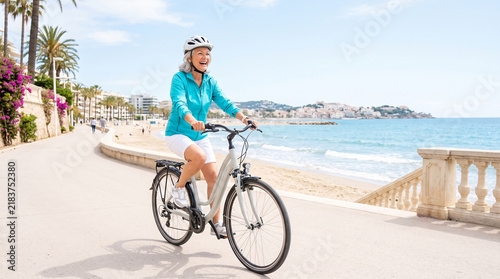 Senior woman riding bicycle along sunny seaside promenade