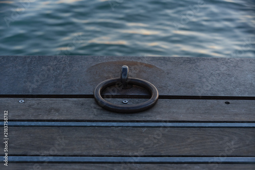 фотографія Close-up of a sturdy steel mooring ring on a wooden dock with calm water ripples in the background at Lake Garda