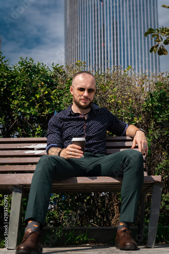 Konstfotografi Man sitting on a bench in a city park enjoying a coffee on a sunny day