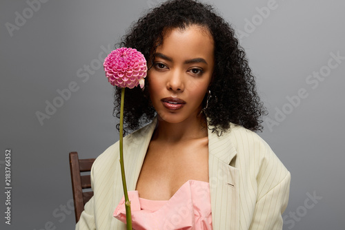 Obraz na płótnie Beautiful young woman poses in stylish attire with flower in a modern studio set