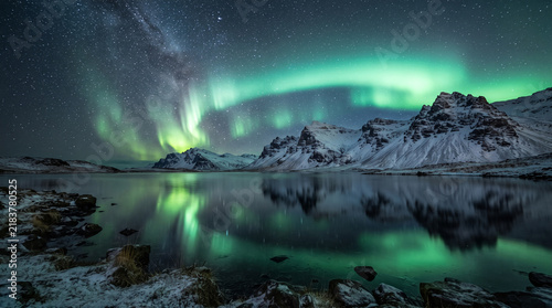 Northern lights over snowy mountain lake with starry night sky and aurora borealis reflection