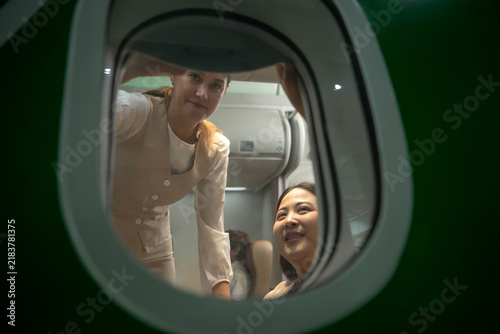 Flight attendant assisting a female passenger inside an aircraft cabin, representing professional airline customer service