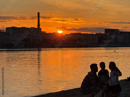 Fotografía A family is sitting on the riverbank at sunset