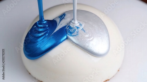Blue and silver glaze being poured over a white dessert, creating a marbled effect on the surface, showcasing the transformation of the sweet treat