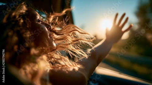 Woman enjoying car ride feeling freedom and wind. Woman feeling the wind on her face and hair while traveling by car at sunset