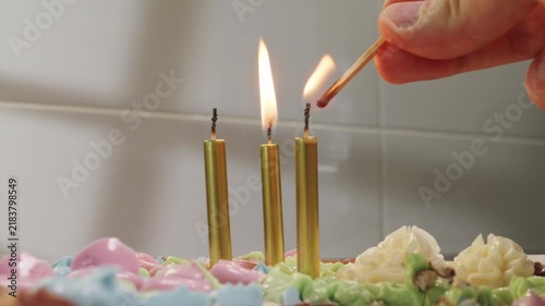 POV shot lighting candles on birthday cake against bright white kitchen background