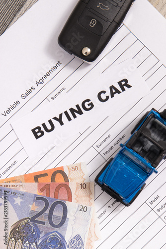 Blue toy car, key, euro banknotes and vehicle sales agreement. Inscription buying car. Sales and buying new or used car