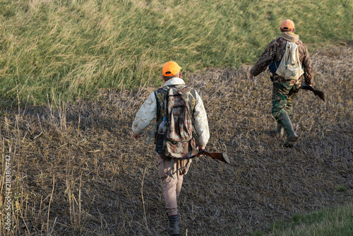 Cuadro en lienzo A hunters in camouflage clothing with a gun in his hands walks along the reeds