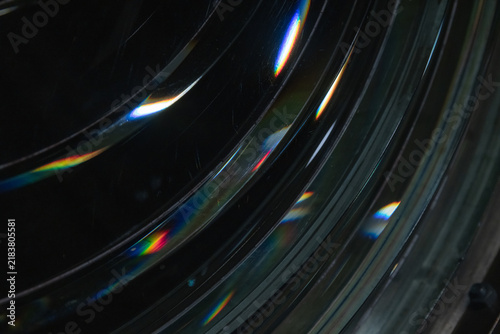 Macro view of a Fresnel lens showing subtle scratches, sleek reflections and colorful rainbow light dispersion. Moody, abstract composition highlighting optics, refraction and modern texture