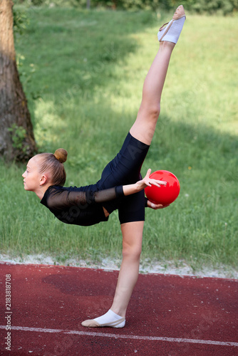 Obraz na plátně Gymnast showcasing flexibility and control outdoors with a red ball, demonstrating skill and fitness