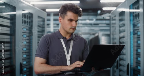 In Data Center, Focused IT Specialist Holds Laptop Inspect Server Racks and Check Network Status. System Diagnostics and Hardware Maintenance Ensure Seamless Cloud Operations. Performance Monitoring.