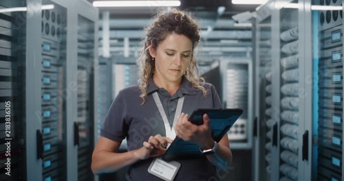 In High Tech Facility, Female Technician Checks Server Telemetry Graphs on Portable Tablet Screen. Cloud Storage Management, Cybersecurity Monitoring Safeguard Critical Enterprise Systems. Portrait.