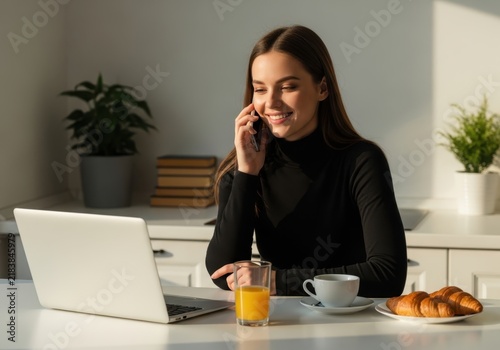 Young woman talking on phone while working on laptop at home