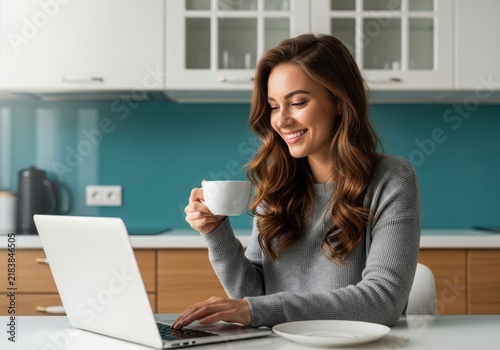 Happy woman working on laptop and drinking coffee in modern kitchen