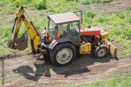 Orange Tractor With Backhoe Working In A Rural Farm Field Earthmoving And Digging Soil