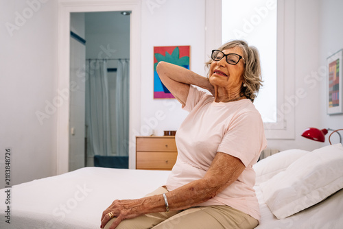 Senior woman suffering from neck pain in bedroom