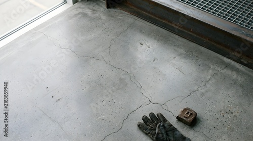 Cracked Concrete Floor and Work Gloves: A close-up view of a damaged concrete floor, featuring visible cracks and wear. A pair of work gloves and a tape measure lie on the surface.