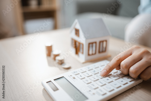 Obraz na płótnie The mortgage calculator evaluates a loan and interest rate as a fingertip presses its white keys by coin stacks, the mortgage calculator assessing a loan and interest rate beside a tiny roofed model