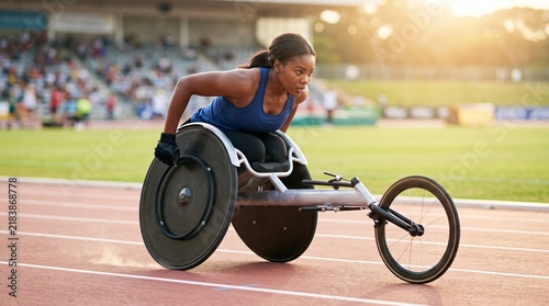 Determination of female paralympic athlete speeding in racing wheelchair along stadium track during sunset, depicting adaptive sports, inclusion, physical endurance, and competitive racing