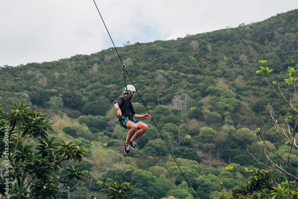 Fototapeta premium Teen boy enjoying thrilling zipline adventure flying over dense tropical rainforest canopy on scenic Mauritius island during active summer holiday vacation trip with extreme outdoor recreation