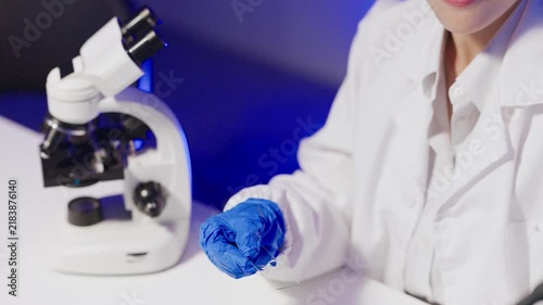 Scientist in Lab Coat Pipetting Sample onto Glass Slide Next to Microscope in Blue Lit Laboratory
