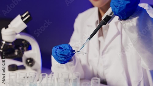 Female Scientist Using Pipette on Glass Slide in Modern Laboratory with Microscope