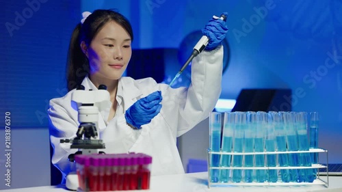Asian Female Scientist Using Pipette with Blue Liquid Test Tubes in Modern Laboratory