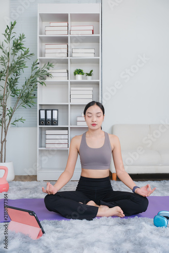 Obraz na plátně Serene Meditation: A young Asian woman finds inner peace and mindfulness as she meditates in a comfortable home setting, her eyes closed and hands resting gently in her lap