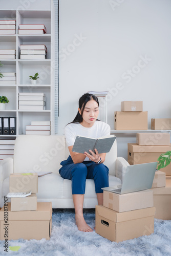 Картината върху платно Startup Entrepreneur at Work: A young woman is diligently working in her home office, surrounded by an organized bookshelf, shipping boxes, and a laptop, ready to fulfill orders and grow her business